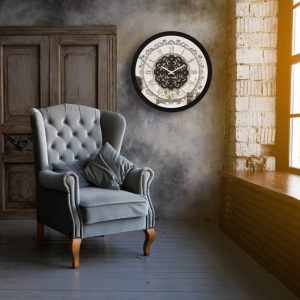 Round black mirrored wall clock hanging in sunlit grey room.