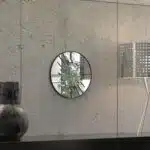 Small round wall mirror with an etched Persian calligraphy design featuring the words 'Women, Life, Freedom,' framed in a gold and black color scheme, hanging on a wall.