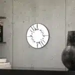 Small round wall mirror with an etched Persian calligraphy design featuring the words 'Women, Life, Freedom,' framed in a gold and black color scheme, hanging on a wall.