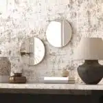 Small round wall mirror with an etched Persian calligraphy design featuring the words 'Women, Life, Freedom,' framed in a gold and black color scheme, hanging on a wall.