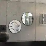 Small round wall mirror with an etched Persian calligraphy design featuring the words 'Women, Life, Freedom,' framed in a gold and black color scheme, hanging on a wall.