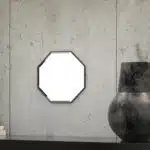 A octagonal wall mirror elegantly mounted on a wall adjacent to a well-stocked bookshelf, enhancing the room's aesthetic appeal.
