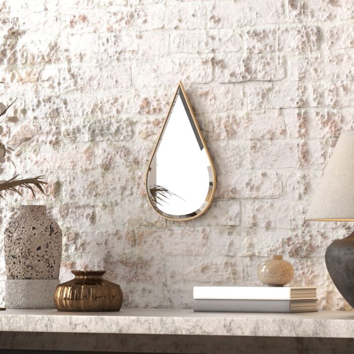 A wall-mounted tear drop shapr mirror reflects a vase and a lamp, creating an elegant and harmonious interior decor scene.