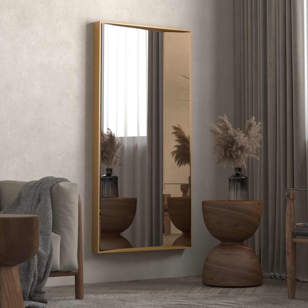 Stylish interior with a gold-framed full-length mirror mounted on a beige wall, reflecting soft natural light. A modern wooden side table with a black vase holding dried pampas grass sits beside the mirror, adding texture and warmth. A cozy armchair with a gray throw blanket partially visible on the left enhances the minimalist, earthy decor